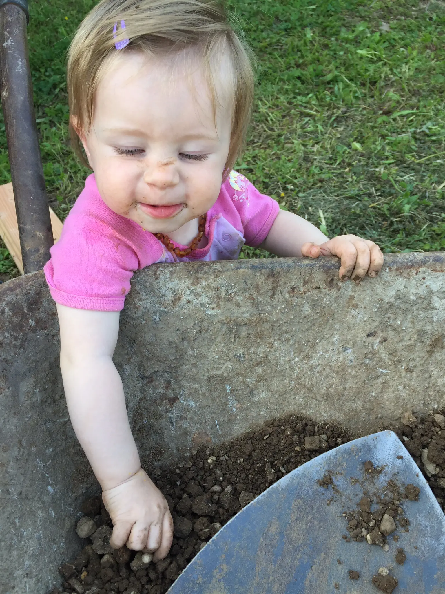 Olivia leaning into a wheelbarrow of dirt and pebbles