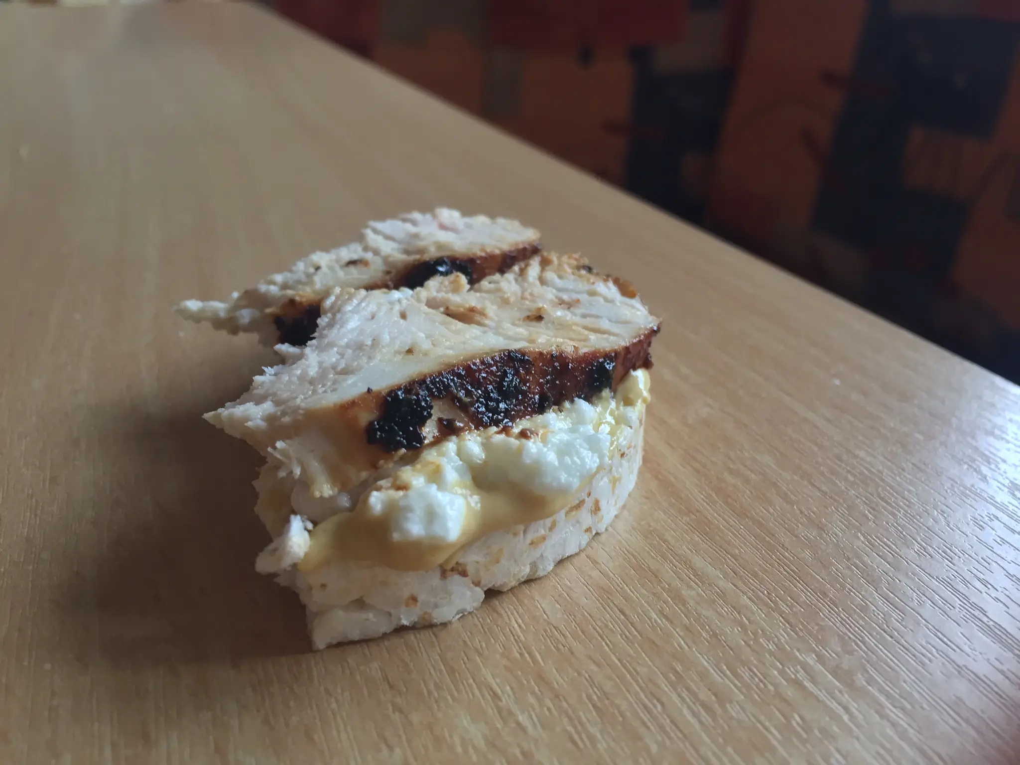 An open chicken rice cake with mustard, cottage cheese, and sliced chicken
