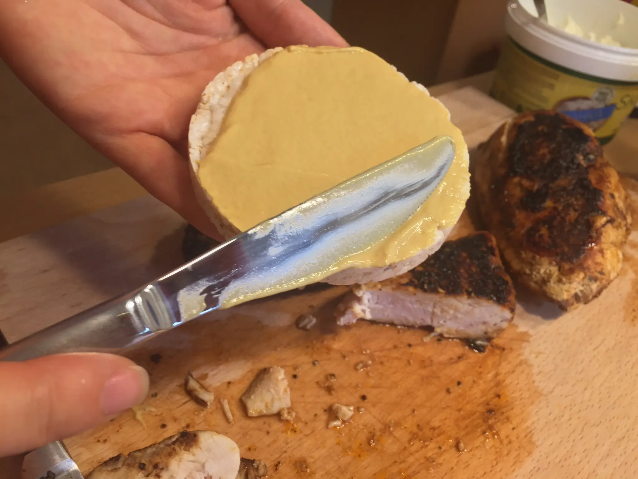 Spreading mustard on a rice cake, cooked chicken on the board